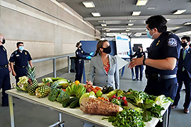 The Secretary and and an individual are standing at a table that is filled with produce.